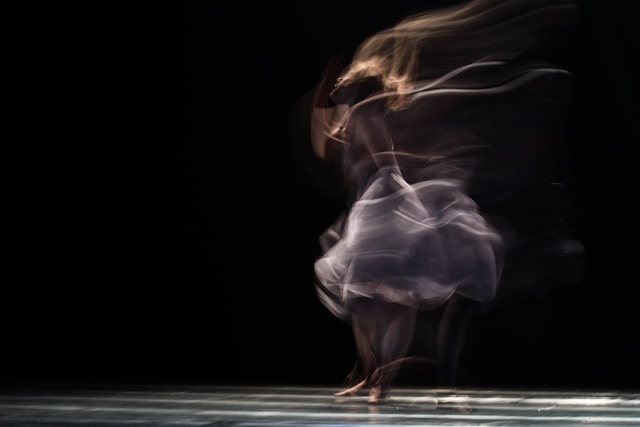 Uma dançarina de balé aparece em um borrão contra um fundo preto. 