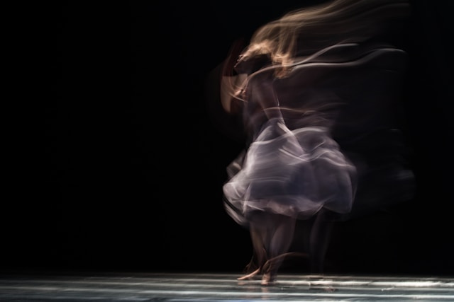 Une danseuse de ballet apparaît dans un flou sur un fond noir. 