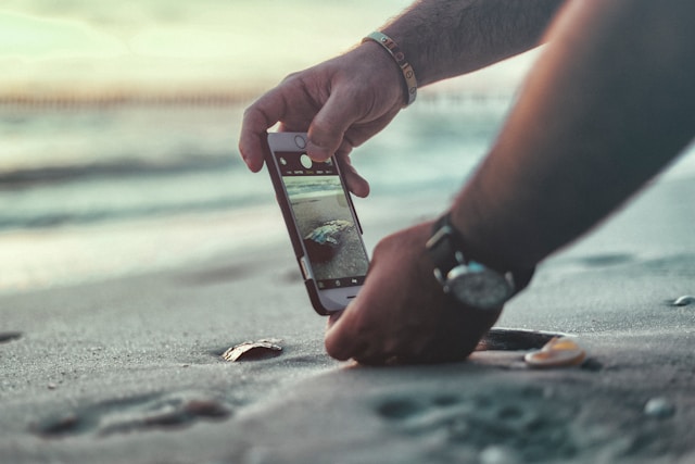 A person uses their phone to take a video of waves crashing on the shore.