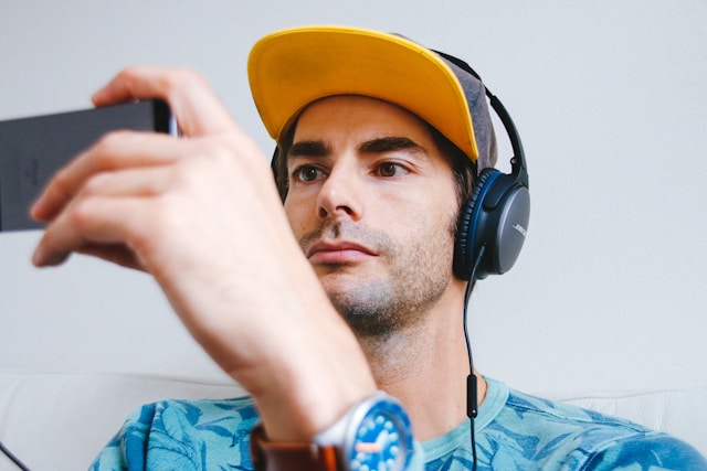 Un uomo con cappellino e cuffie guarda i video di TikTok sul suo telefono. 