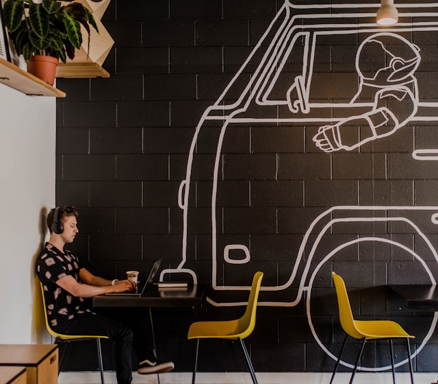Een persoon gebruikt zijn laptop in een café naast een muur met een tekening van een robot in een busje. 