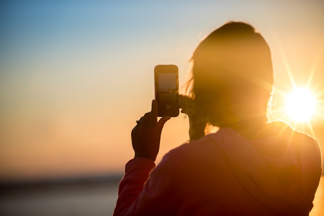 A woman takes a video of the ocean during sunset using TikTok’s camera. 
