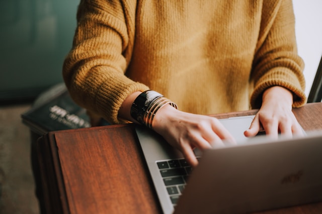 A person sits on their desk and types on their laptop.