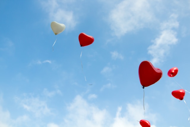 Red and white balloons float towards the clouds. 
