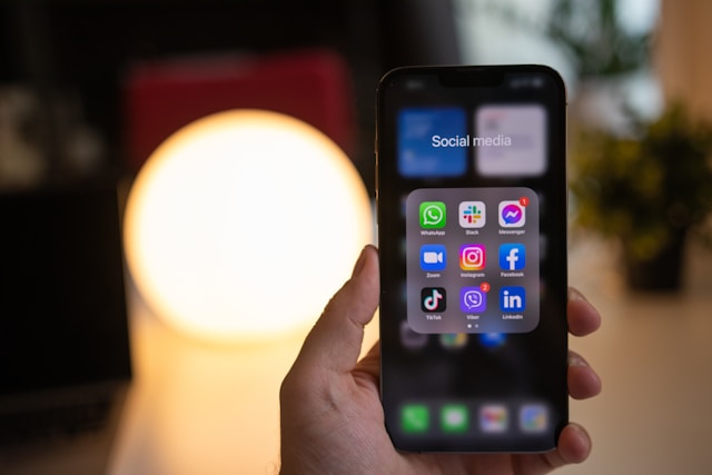 A phone screen in a person’s hand displays various social media apps. 