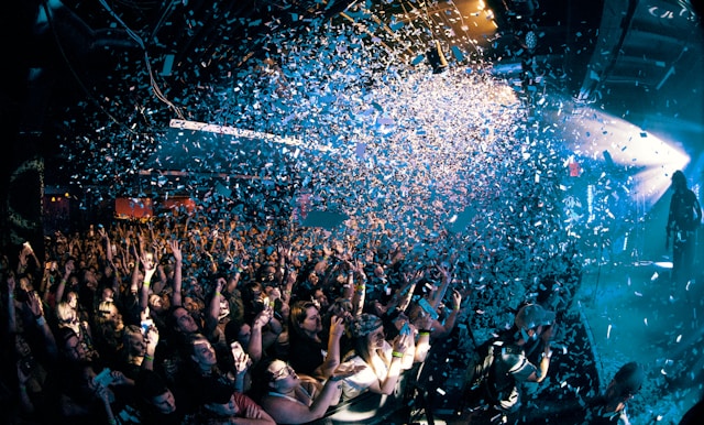 Des confettis colorés tombent sur un grand groupe de personnes réunies pour une performance. 
