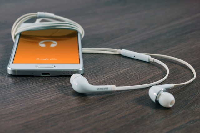 A white phone and a pair of earphones rest on a table. 
