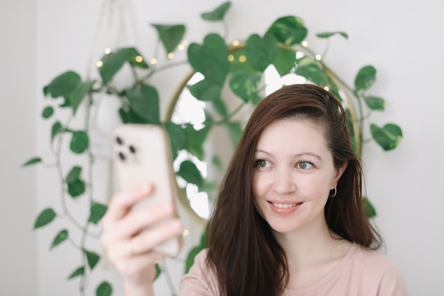 A young woman takes a selfie for Instagram using her phone. 
