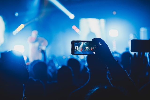 Uma pessoa em um show lotado usa seu celular para gravar o artista no palco.