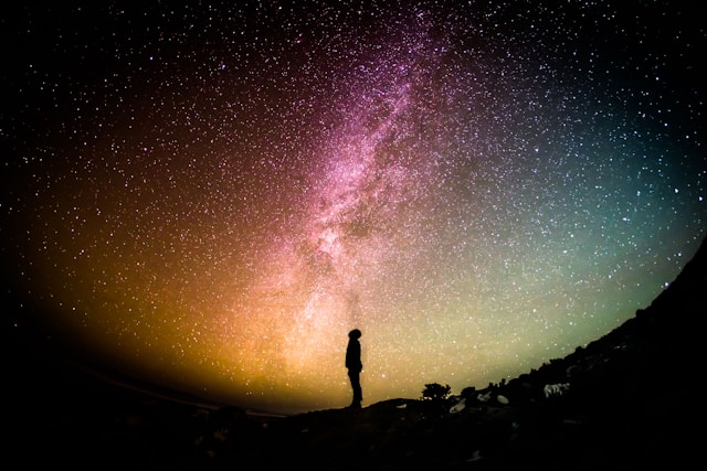 A person is silhouetted against the bright stars of the Milky Way at night.
