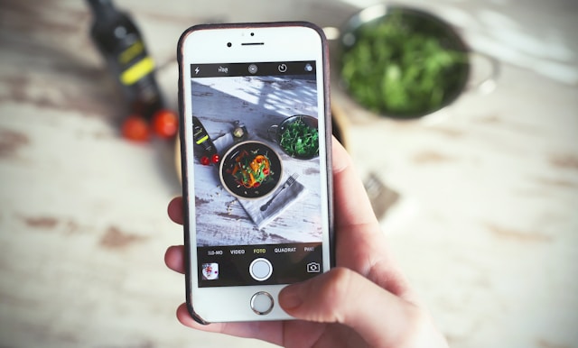 A person takes a photo of a salad on a table using a phone camera. 
