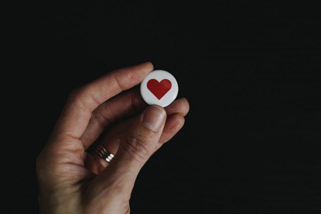 Een hand houdt een kleine witte knop vast met een rood hart erop. 