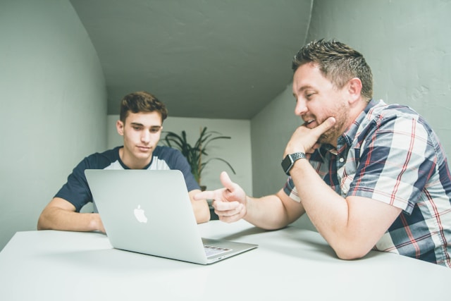 Un père et son fils sont assis devant un ordinateur portable et discutent de la sécurité en ligne. 