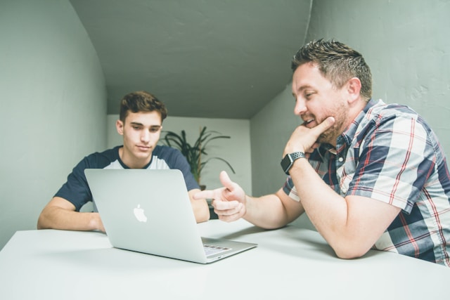 Een vader en zoon zitten voor een laptop en bespreken online veiligheid. 