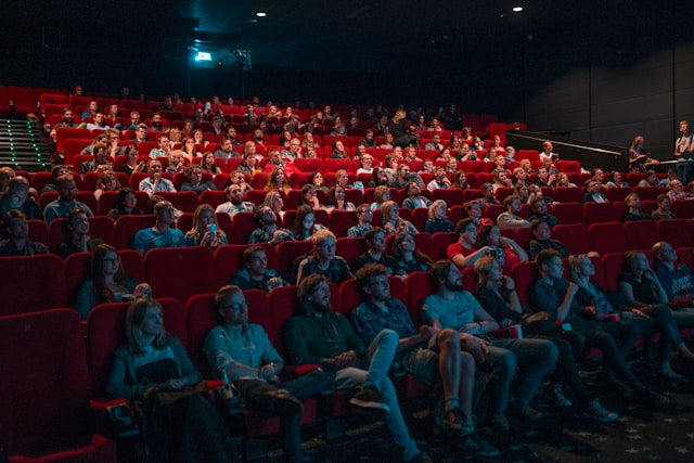 Kijkers zitten op rode stoelen in het theater. 