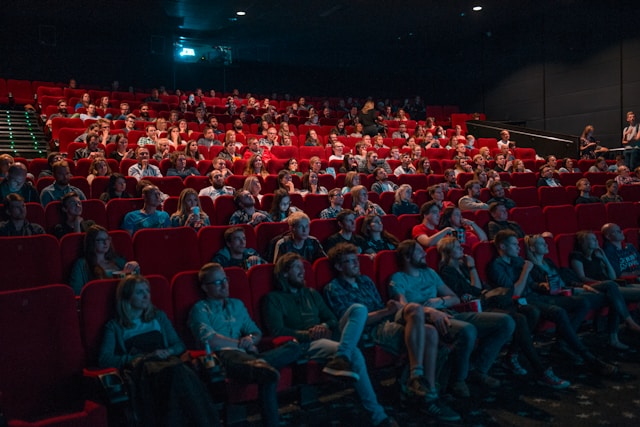 Viewers sit on red chairs at the theater. 
