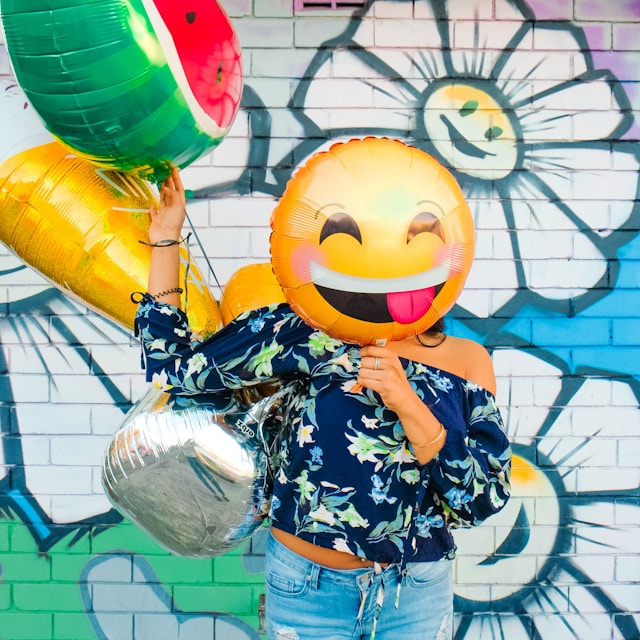 Uma mulher segura um balão amarelo sorridente em frente ao seu rosto.  