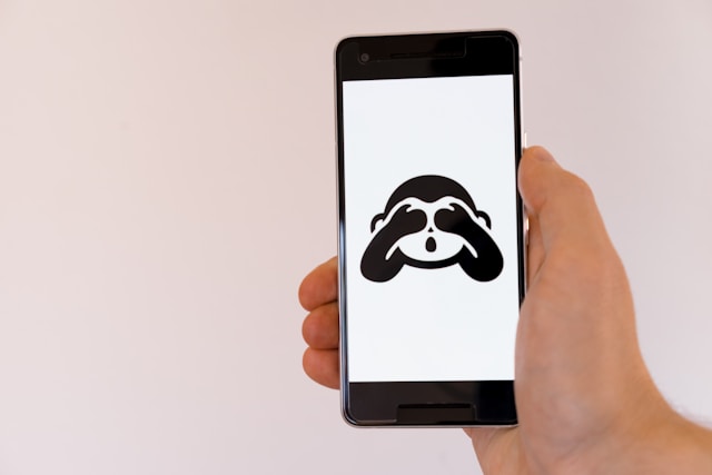 Een telefoonscherm toont een aap met zijn handen over zijn ogen. 