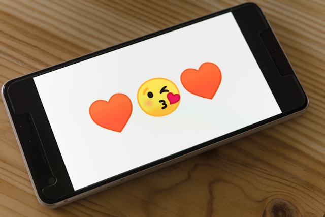 A phone screen displays a kissing emoji between two red heart emojis.