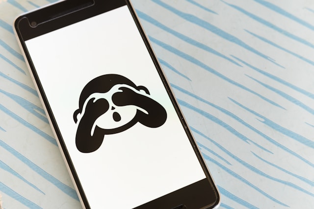 A phone screen displays a black and white monkey with its hands over its eyes. 