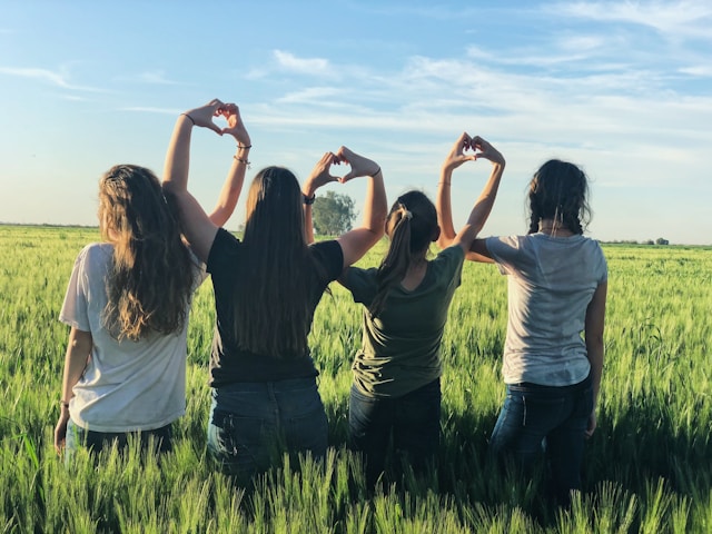 Quatre amies se tiennent dans un champ d'herbe et font des signes de cœur avec leurs mains. 