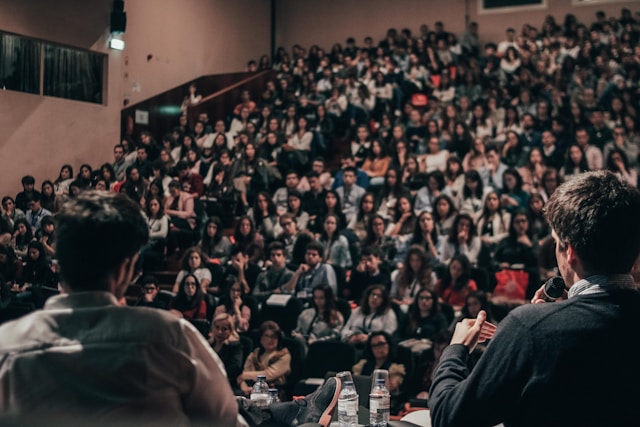 A big audience listens intently to two speakers on stage. 
