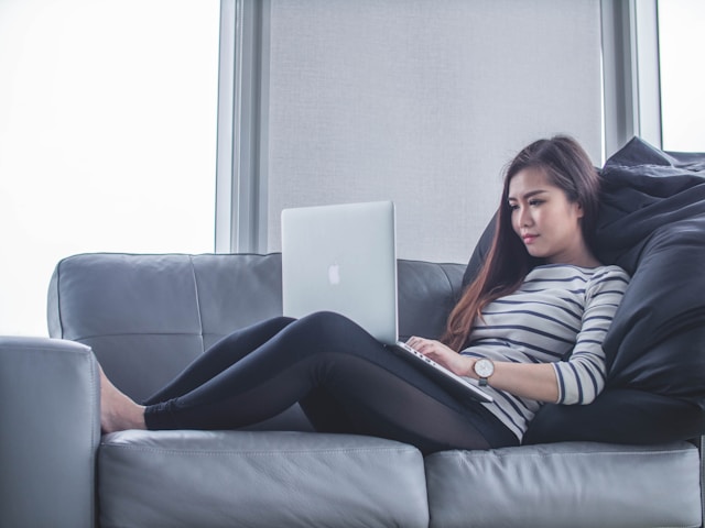 Een vrouw ligt op een bank terwijl ze haar laptop gebruikt. 