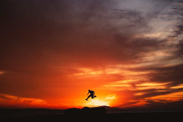 A wide shot of a person jumping high as the sun sets in the background.