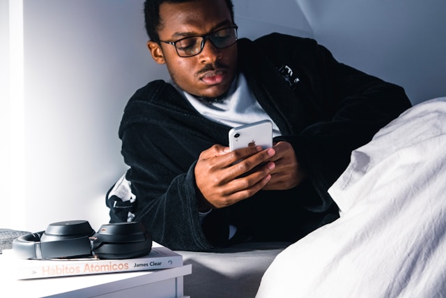 Ein Mann surft auf seinem Handy, während er im Bett liegt. 
