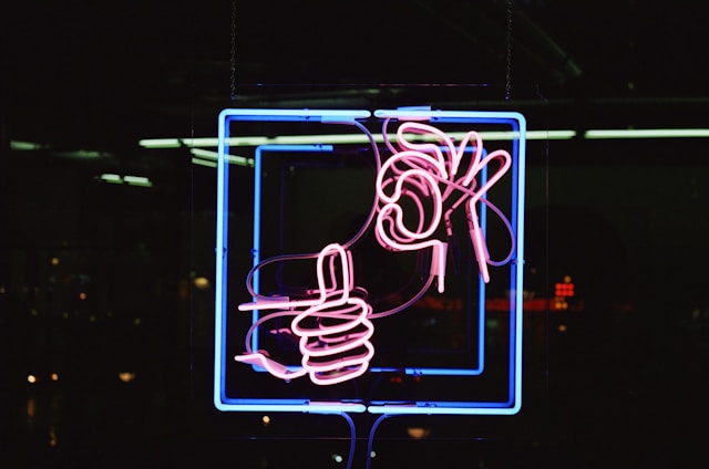 Un néon rouge montre une main qui lève le pouce et une autre qui fait le signe "ok". 