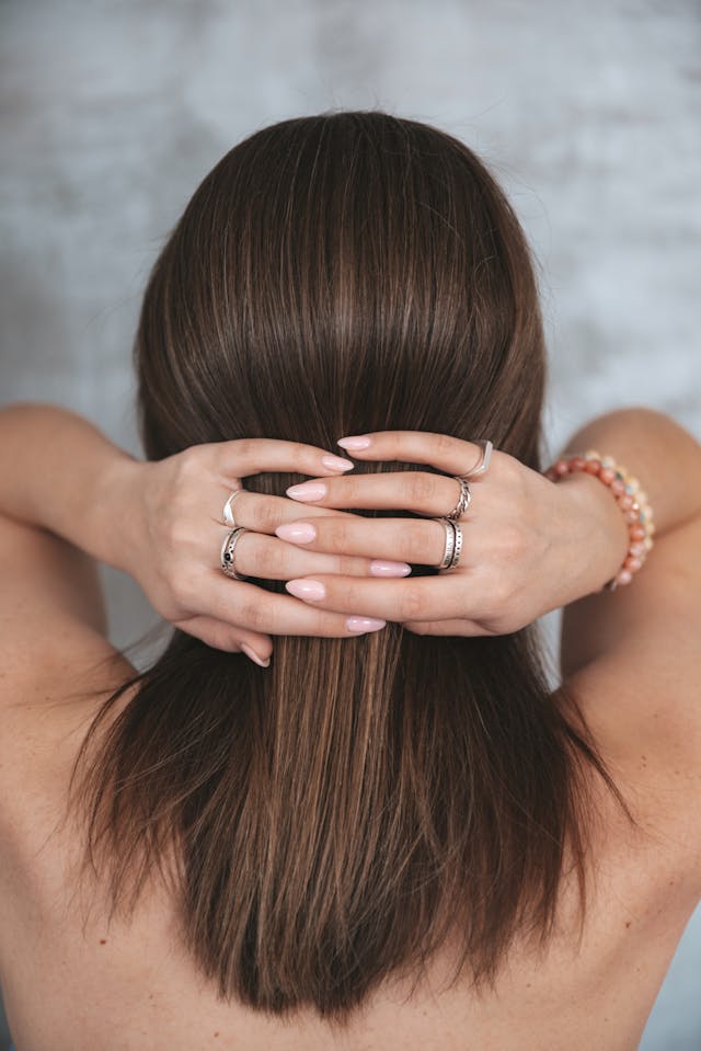 A woman’s hands at the back of her head showing pink nails.
