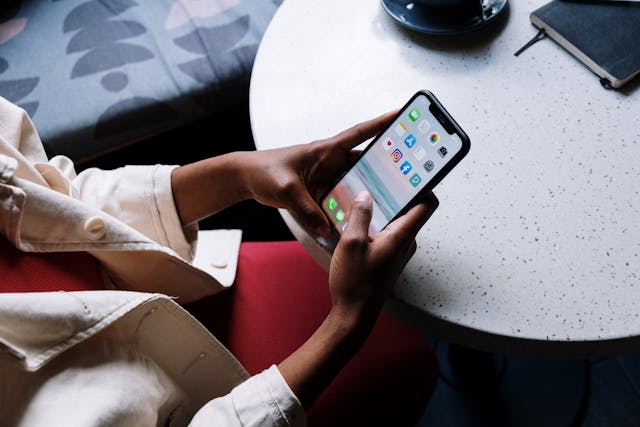 A person holds a phone showing the home screen.
