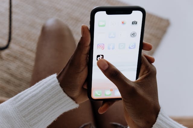 Una persona con un iPhone nero seleziona l'app TikTok dalla schermata iniziale.
