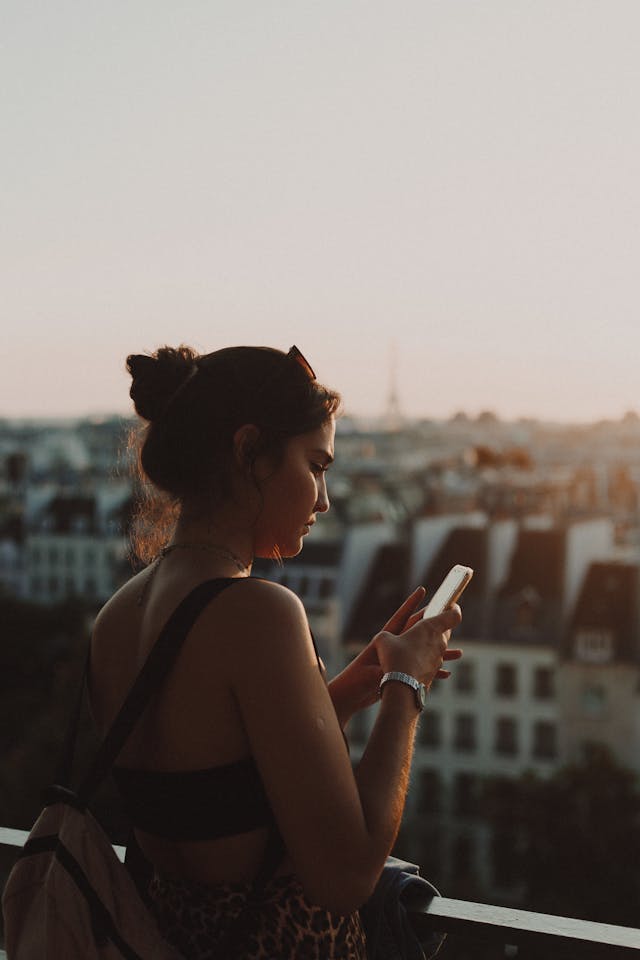 Een vrouw staat op een balkon en bladert door haar mobiele telefoon.