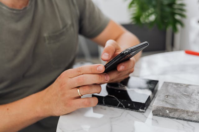 Eine Person sitzt an einem Schreibtisch mit ihrem Handy.