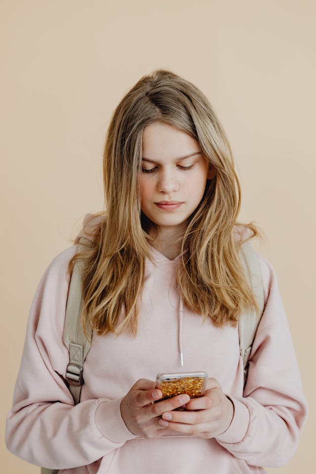 Una ragazza con una felpa rosa con cappuccio scorre sul suo telefono.