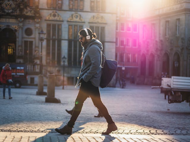 A man with headphones crosses the street.