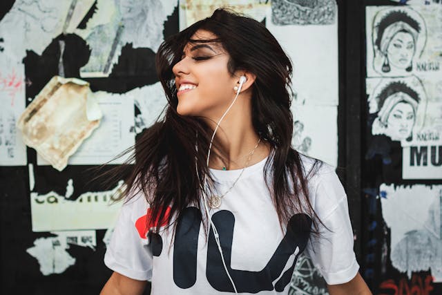 A woman smiles as she listens to audio through her wired headphones.