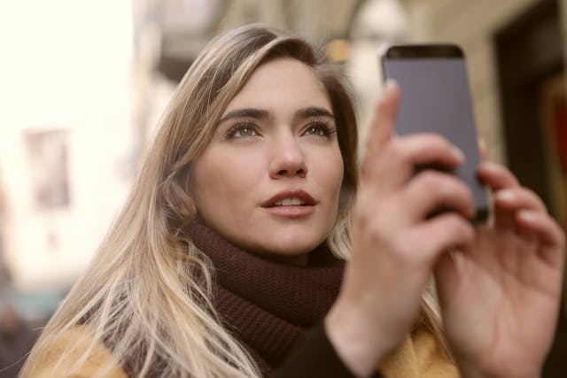 Una donna alza il telefono per registrare qualcosa in lontananza.