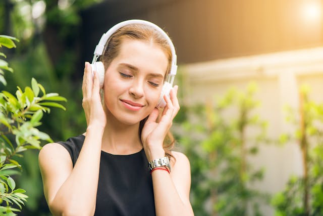 A woman smiles as she listens to sound from her white headphones.
