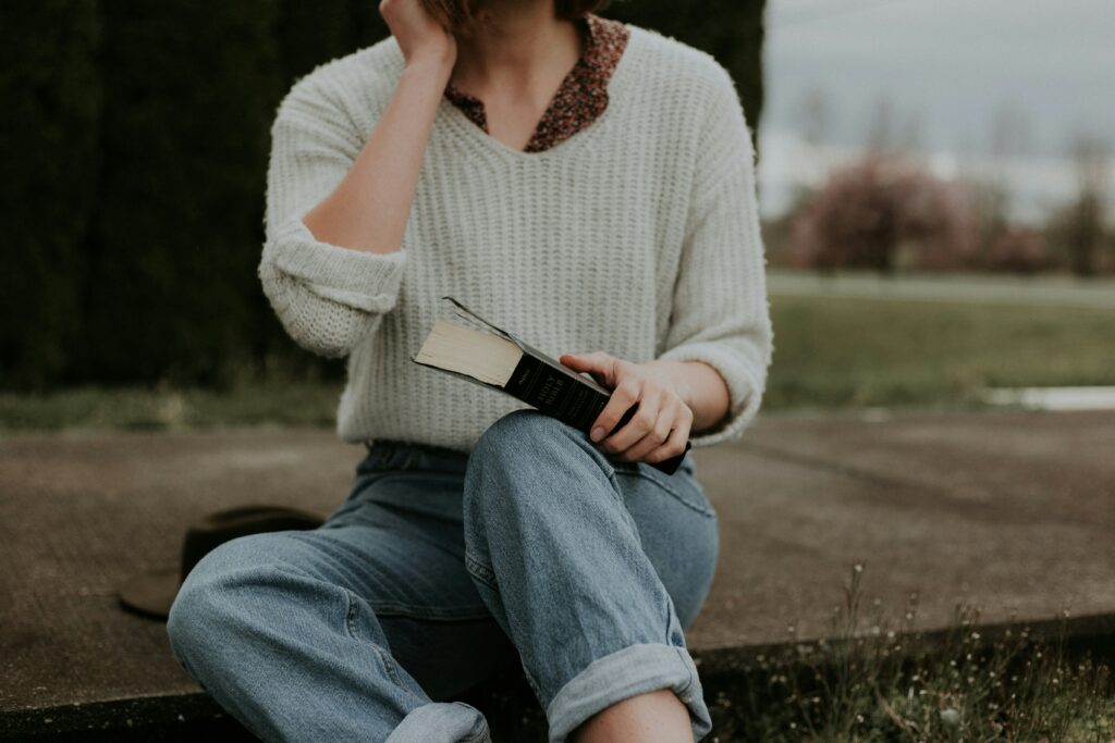 Ein Bildausschnitt einer Frau in Jeans und einem Pullover über einer geblümten Bluse.