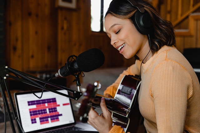 A woman records her music as she sings and plays her guitar.