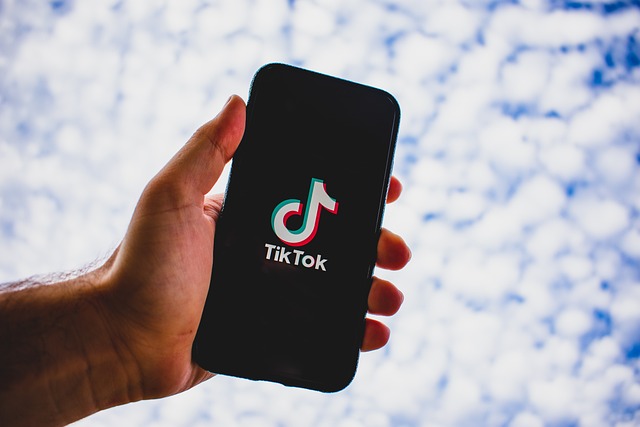 在厚厚的云层下，一个人拿着显示 TikTok 徽标的手机。
