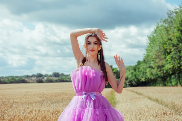 A model wears a bright pink tube and tulle dress in a field of grass. 
