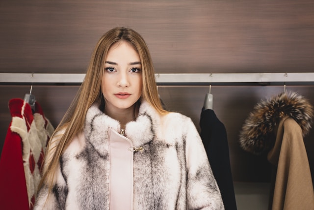 A woman in a white fur coat stands in front of a rack of coats. 