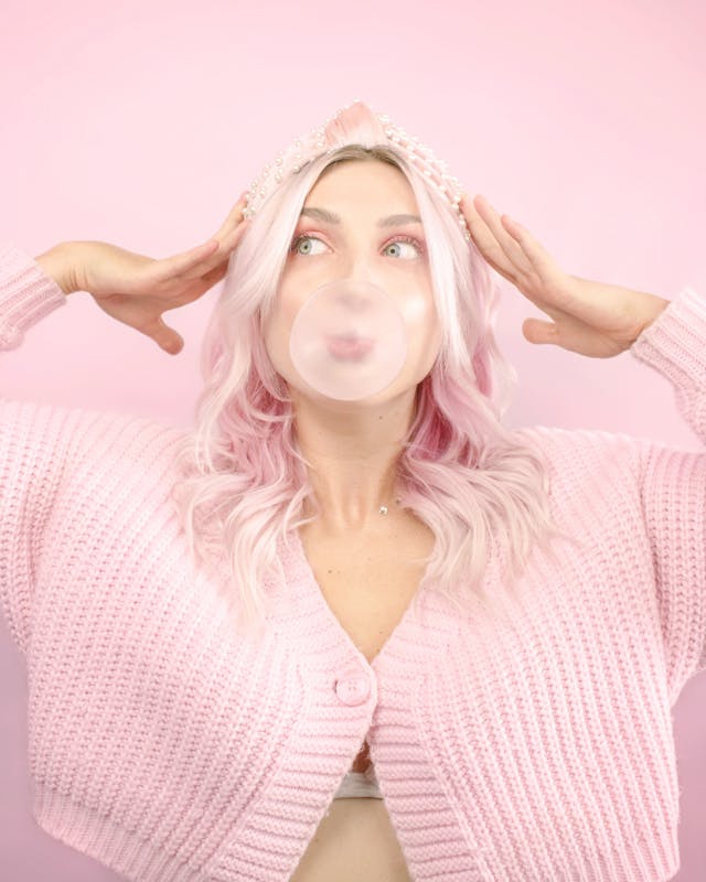 A woman wears a pink cardigan and pearl headband.