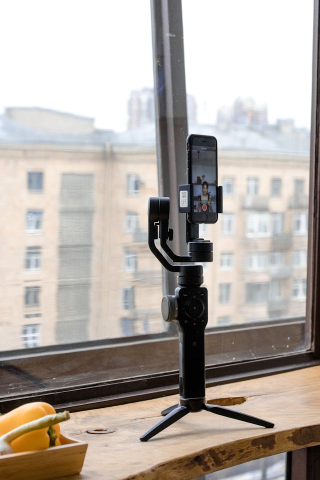 A phone in front of a window records a woman.
