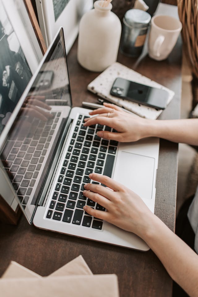 A person types on their laptop with their phone next to them.