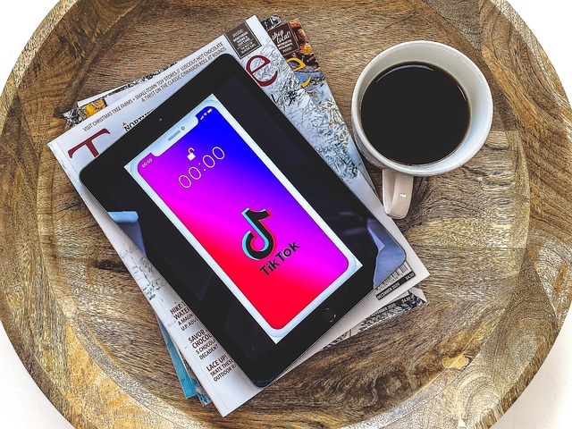 Le logo TikTok apparaît sur une tablette posée sur une pile de magazines, avec une tasse de café à côté.