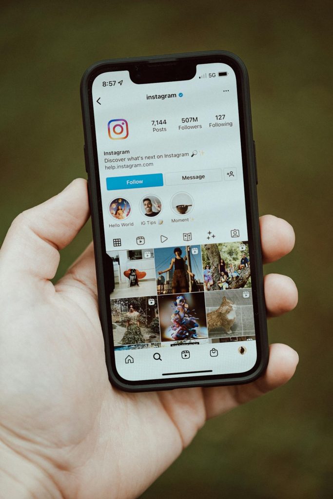 A hand holding a phone showing Instagram’s profile with 507M followers on the screen.
